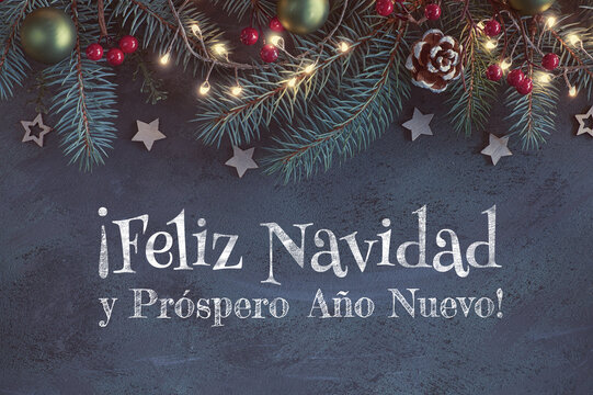 Christmas background with fir twigs, red berries, cones and garland with Xmas lights on dark abstract background. Feliz Navidad means Merry Christmas in Spanish language.