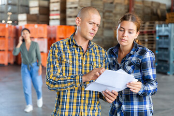 Man and young woman talking about documentation while standing in warehouse. Another woman talkin...