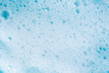 Texture of white foam on blue background. Foam cosmetic product for skincare procedure. White foam texture macro background. Cosmetic product foamy smudges with bubbles. Foamy skin care product