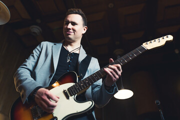 Musician playing on a guitar. Caucasian mid adult man in a rock band playing his guitar. Stage lightening. Low angle indoor shot. High quality photo