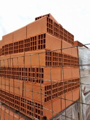 Ladrillos huecos de cer&agrave;mico rojo en el corral&ograve;n de venta de materiales para la construcci&ograve;n, con c&agrave;mara de aire antihumedad,  forma un original dise&ntilde;o constructivo con fondo del cielo nuboso 