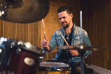young dark-haired drummer playing happily while rehearsal in the studio, modern music band. High...