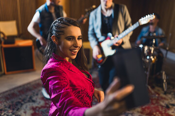 Playful woman vocalist in vivd pink blazer takes a selfie with guitarists and drummer during one of their practice performances. High quality photo