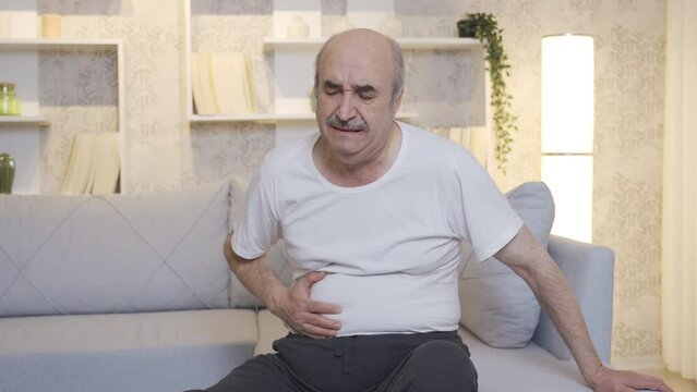 Sick old man has stomach ache. Pancreatic Cancer.
The old man is sitting on the sofa at home and has stomach ache. Pancreas, stomach poisoning, chills.
