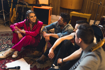 Fototapeta na wymiar Excited band members sitting together on a carpet. Female vocalist talking to her band partners about a new song idea. High quality photo