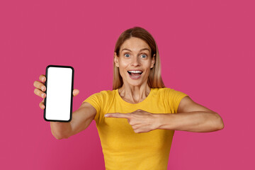 Naklejka premium Glad surprised inspired mature caucasian blonde woman in yellow t-shirt with open mouth point finger at smartphone
