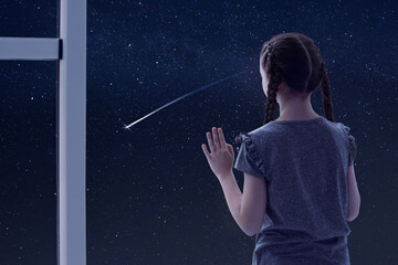 Little girl near window looking at shooting star in beautiful night sky