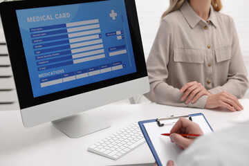 Doctor using computer to fill out patient's medical card at table in clinic, closeup