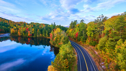 Aerial over road next to blue lake and surrounded by fall forest