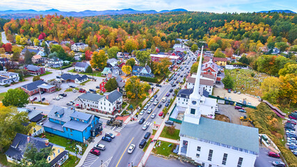 Stunning aerial over small Vermont town of Stowe surrounded by fall foliage and focus on white...