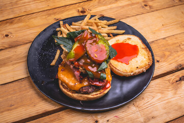 Hamburguesa de carne con queso, papas a la francesa, vegetales sobre un plato negro, acompañado de cerveza clara en un tarro.