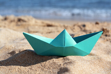 Fototapeta na wymiar Green paper boat near sea on sunny day, closeup