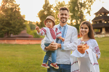 Happy cute family in embroidered Ukrainian shirts with korovai bread on sunny day. Space for text