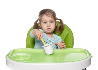 Cute little child eating tasty yogurt from plastic cup with spoon in high chair on white background