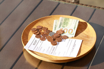 Wooden plate with payment for order and receipt on table, closeup. Leave tip