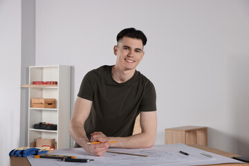 Young handyman working with blueprints at table in room