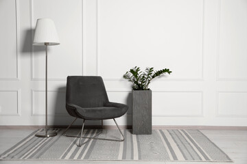 Cosy armchair, floor lamp and potted plant near white wall in room, space for text. Interior design