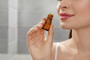 Fototapeta premium Young woman smelling essential oil indoors, closeup
