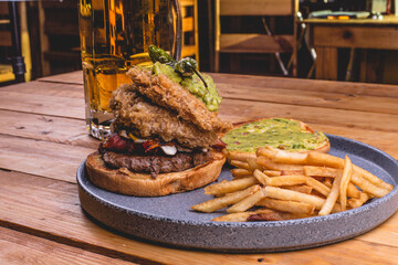 Hamburguesa de carne con queso, papas a la francesa, vegetales sobre un plato negro, acompañado de...