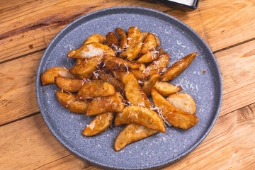 Plato de papas gajo con queso sobre una mesa de madera.