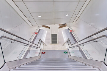 Modern clean white subway station stairs leading down to tracks with red and green arrow markers