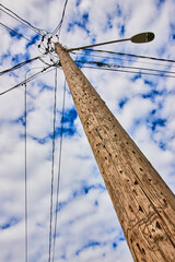 Detail looking up textured wood telephone pole with spotty clouds on blue sky
