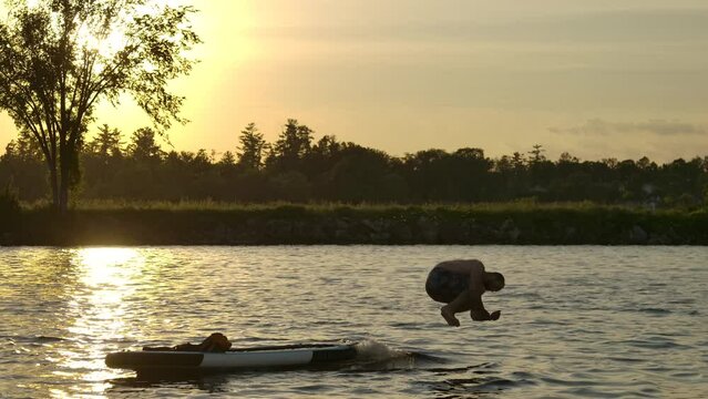 playful guy jumps off paddleboard cannonball into lake slomo sunset funny