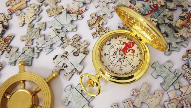 Golden compass pointing for directions and a rudder wheel turned left and right with jigsaw puzzles of world map lying around.