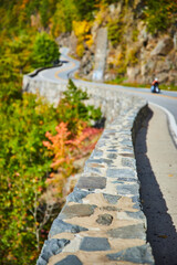 Stone wall and road winding through mountain cliffs with biker going through and focus on foreground