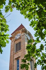 Green leaves frame limestone clock tower on college campus