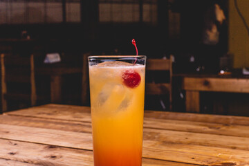 Colorida bebida de tequila con jugo de naranja, sangría y cereza, sobre una mesa de madera