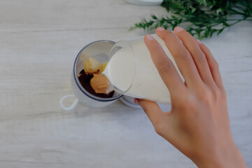 Close-up of a woman pouring milk into a small portable blender to make a smoothie