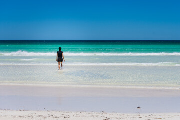 Lone woman walking into the water on beach. Crystal clear water. Peaceful solitude on Australian beach. Blue sky, turquoise coloured water. 