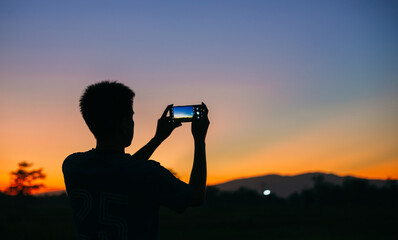 Silhouette man takes photo of the mountain landscape with his smart phone, a view from the back. travel in summer, outdoor activities