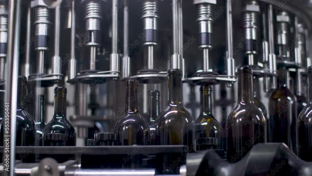Poster wine bottling machine - empty glass bottles being filled with wine in automatic machinery. closeup