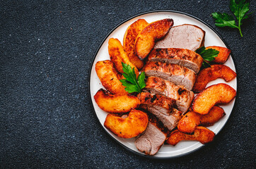 Fried pork tenderloin with quince or apple slices served on plate. Black table background, top view