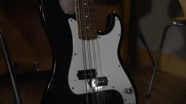 Black White Bass Guitar Resting On Stand Inside Studio. Slow Tilt Up