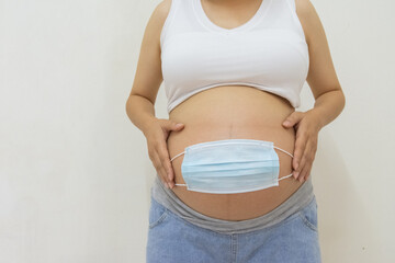 Pregnant woman holding medicinal face mask on her pregnant belly abdomen. Coronavirus covid19 new normal rules and regulations, isolation and new lifestyle concept