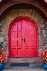 Fototapeta na wymiar Stunning vibrant red arched double doors with stone arch and pair of red plants in blue pots
