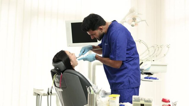 Beautiful smile with white teeth. Bearded male dentist treating teeth of a young asian woman using tooth drill and magnifying glass in the dental office.