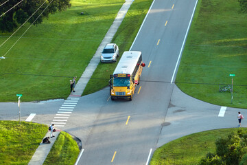 Top view of standard american yellow school bus picking up kids at rural town street stop for their lessongs in early morning. Public transport in the USA - obrazy, fototapety, plakaty