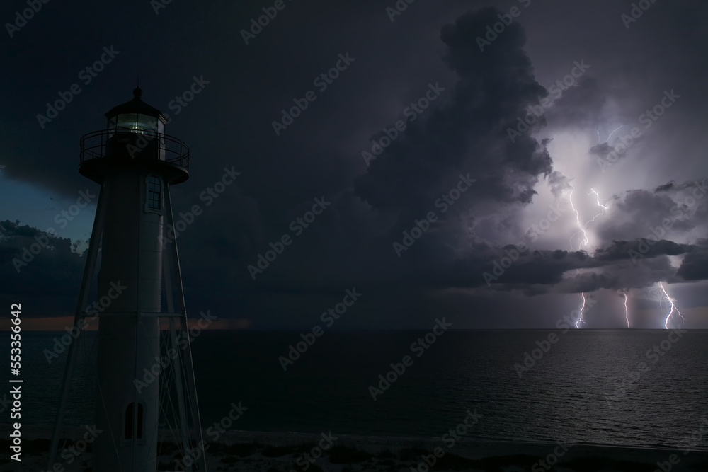 Wall mural white tall lighthouse on sea shore with blinking light at stormy night for commercial vessels naviga