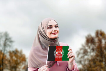 Muslim woman in hijab holds flag of Afghanistan
