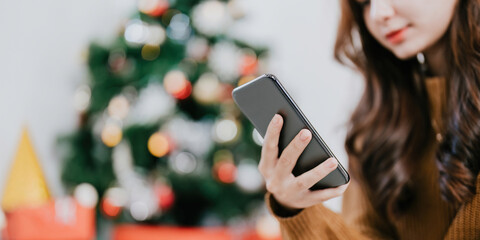 Close up hand of woman using her Mobile Phone at home. Boke christmas tree background