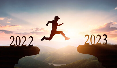 2023 New Year's concept: Man jumping on cliff 2023 over sunset sky background. 