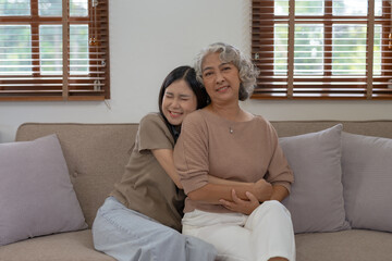 Asian mother and daughter spend the holidays in their living room, expressing their love by embracing each other at home happily and warmly.