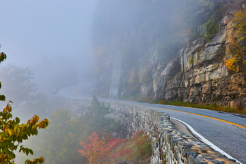 Stone wall along stunning road against cliffs winding away into fog