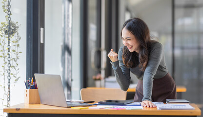 Happy excited successful business asian woman triumphing in office, Portrait of a cheerful Asian businesswoman sitting at the table in office, 	