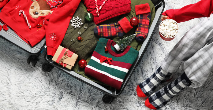 Woman with cup of hot chocolate packing suitcase at home, top view. Christmas holidays concept