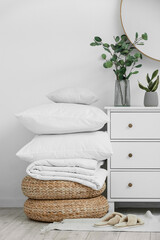 Folded blanket and pillows on poufs near light wall